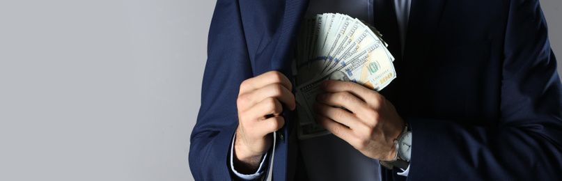 Man putting bribe into pocket on grey background, closeup. Banner design