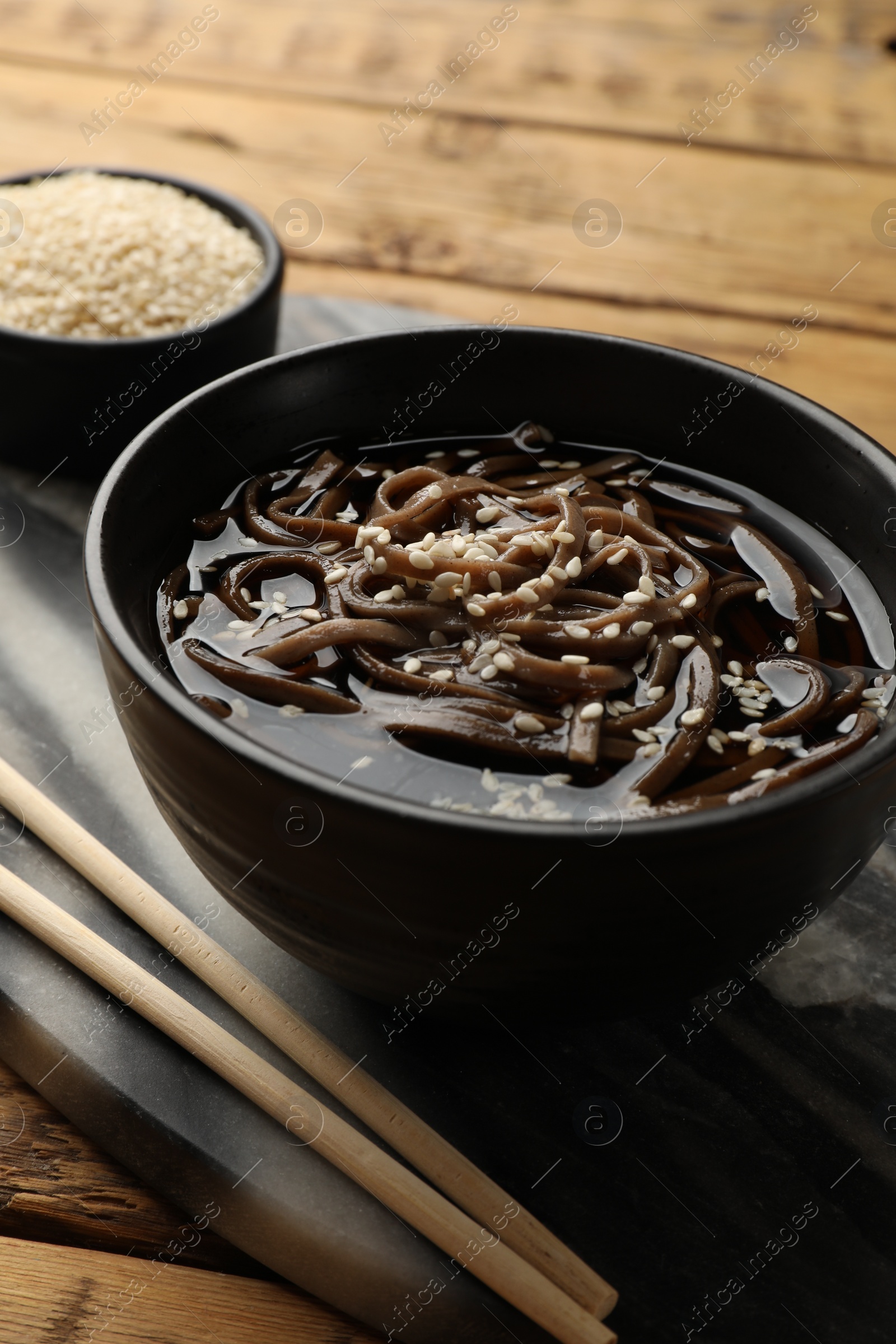 Photo of Tasty soup with buckwheat noodles (soba), sesame and chopsticks on table, closeup