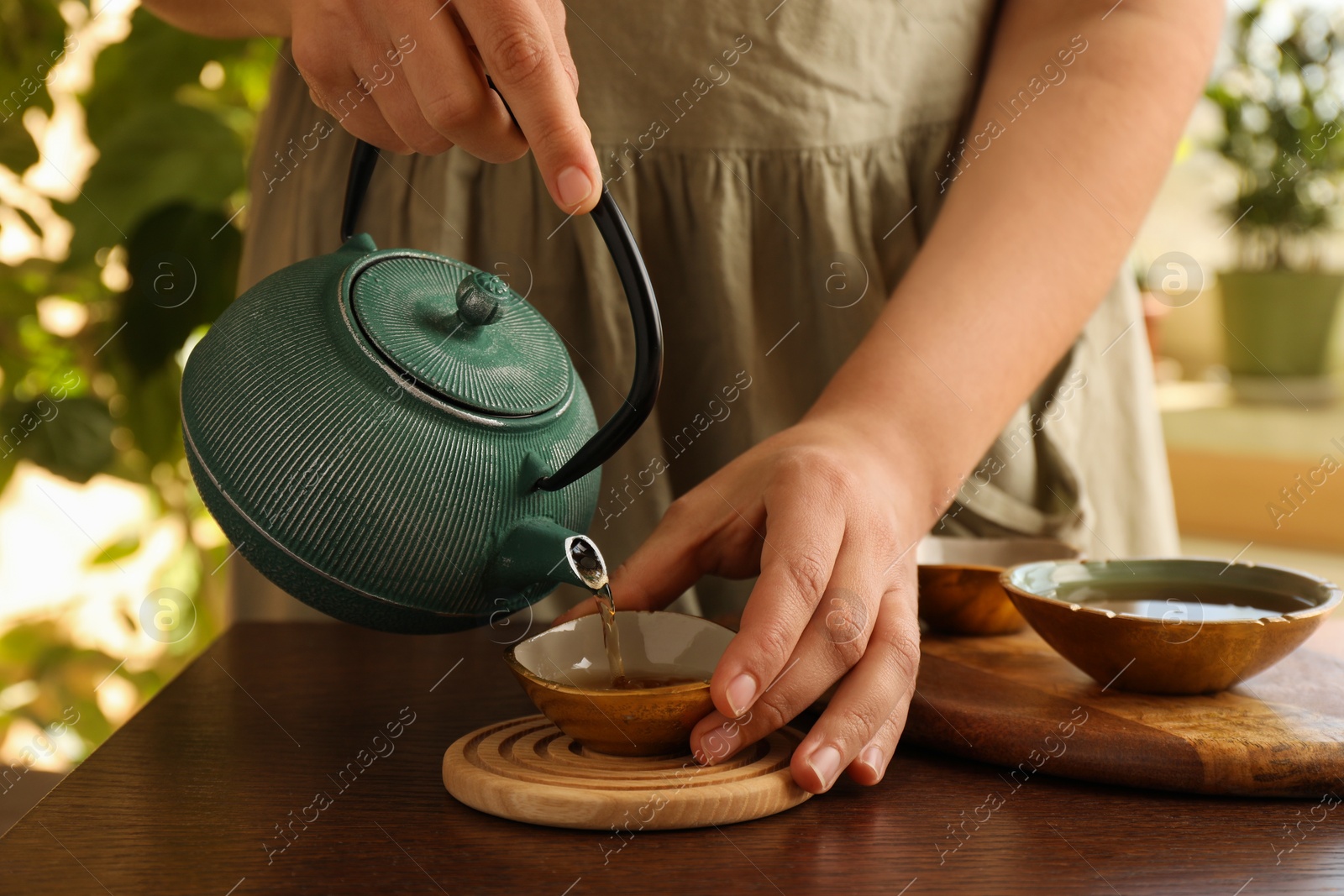 Photo of Woman pouring freshly brewed tea from teapot into cup at wooden table indoors, closeup. Traditional ceremony