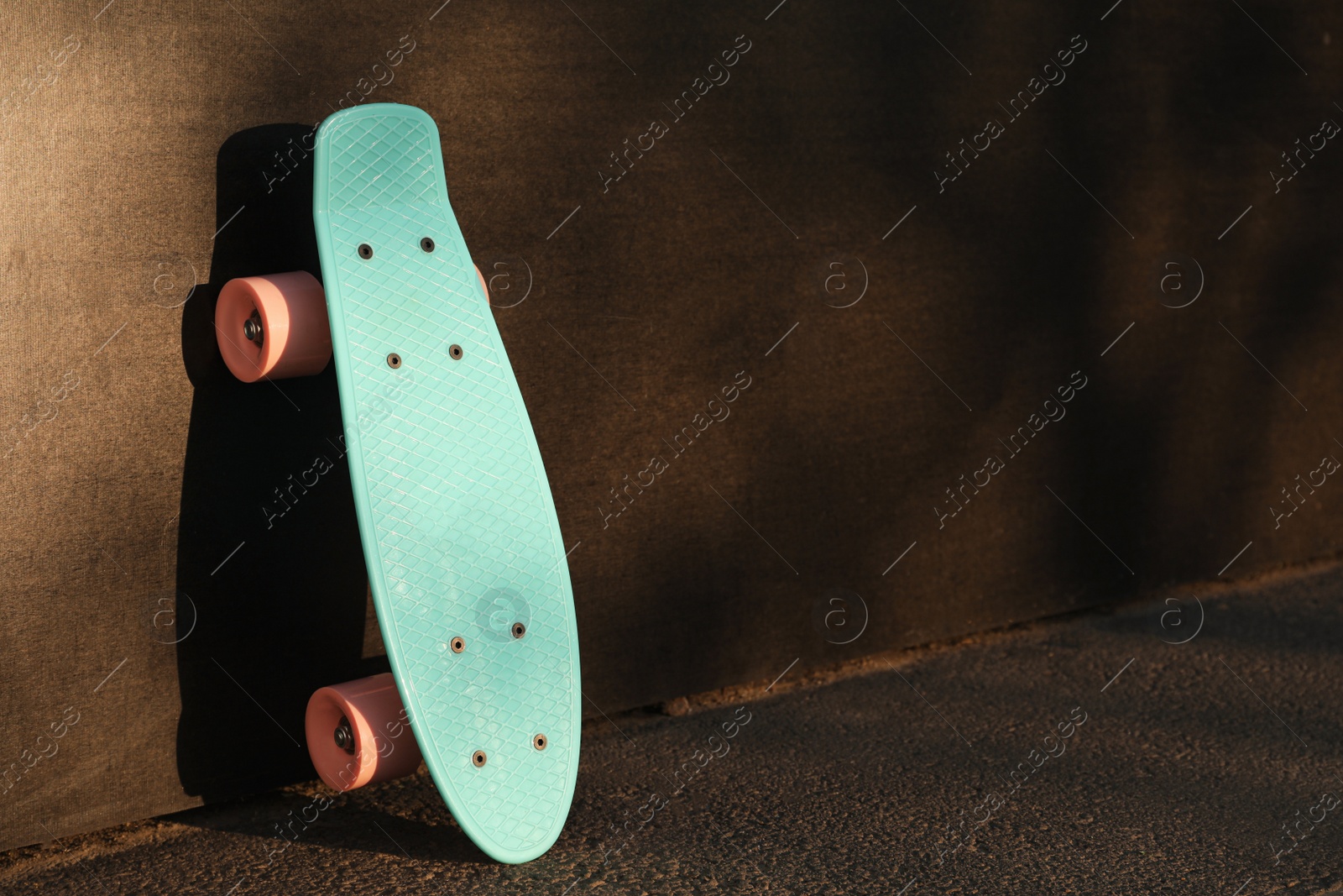 Photo of Modern light blue skateboard with pink wheels near black wall outdoors. Space for text