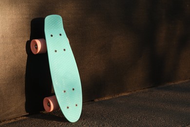 Modern light blue skateboard with pink wheels near black wall outdoors. Space for text