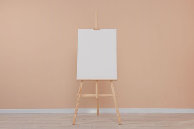 Photo of Wooden easel with blank canvas near beige wall indoors.