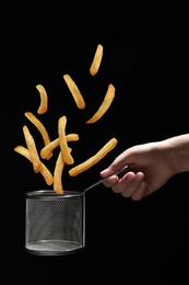 French fries falling into metal basket held by woman on black background, closeup