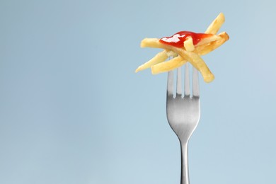 Photo of Fork with tasty french fries against light blue background, closeup. Space for text