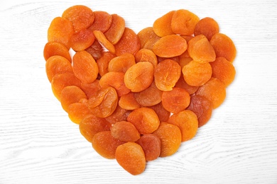 Photo of Heart shaped heap of dried apricots on white wooden table, top view. Healthy fruit