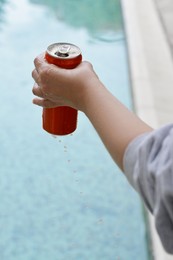 Photo of Woman holding tasty open canned beverage near swimming pool, closeup