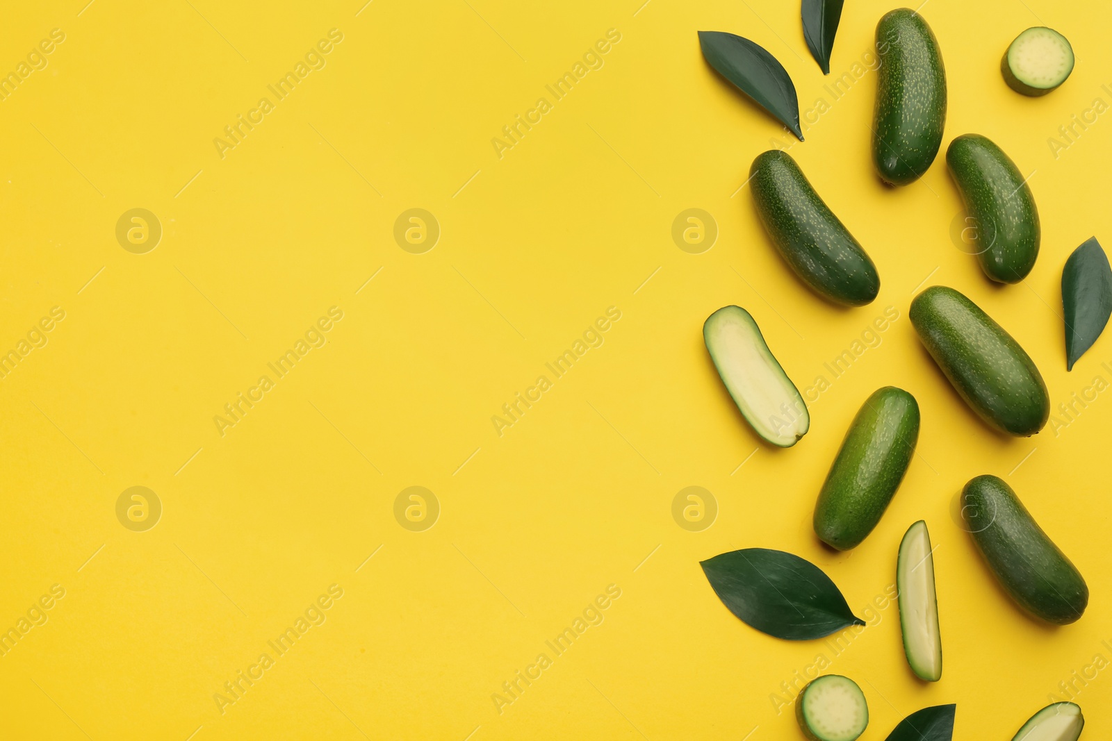 Photo of Whole and cut seedless avocados with green leaves on yellow background, flat lay. Space for text