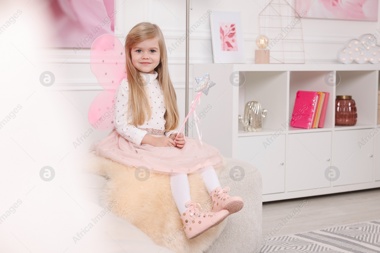 Photo of Cute little girl in fairy costume with pink wings and magic wand at home, space for text