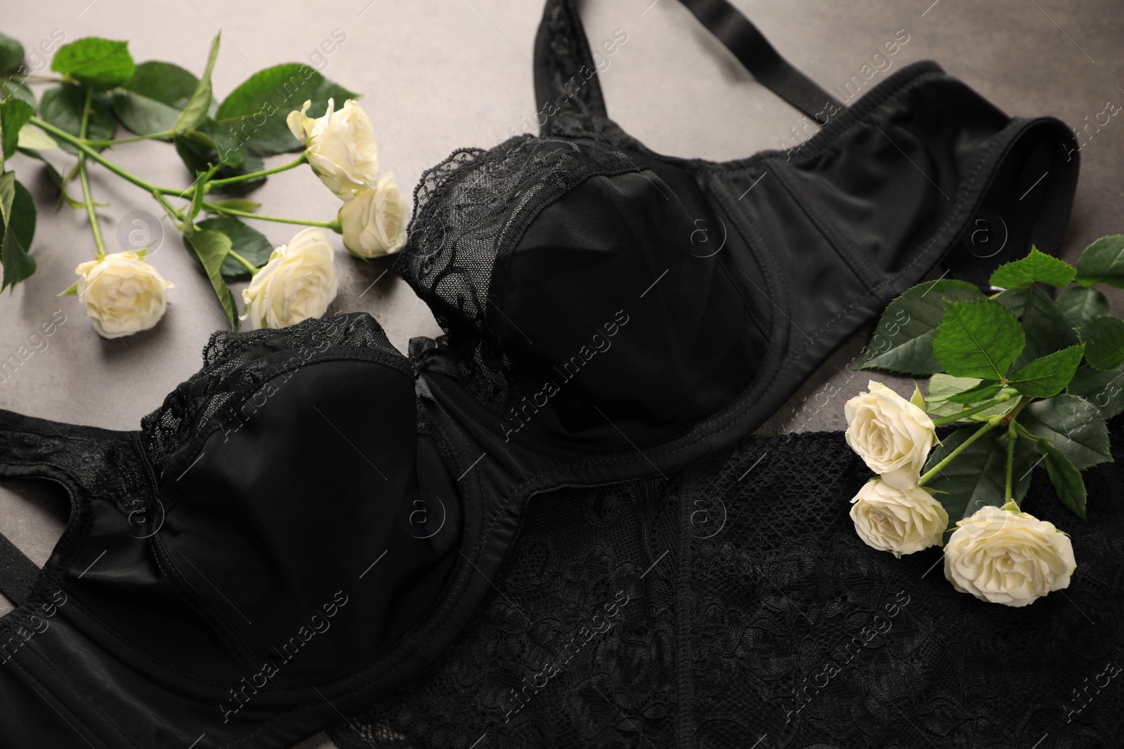 Photo of Elegant black plus size women's underwear and beautiful roses on grey background, closeup