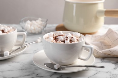 Photo of Aromatic hot chocolate with marshmallows and cocoa powder served on white marble table, closeup