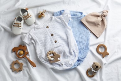 Flat lay composition with cute baby clothes and accessories on white bedsheet