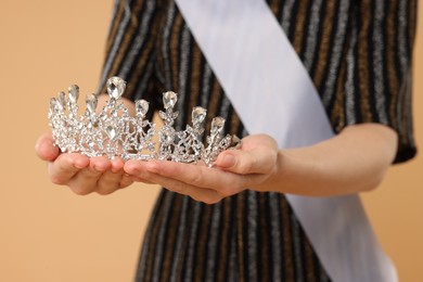 Photo of Woman holding beautiful tiara on beige background, closeup