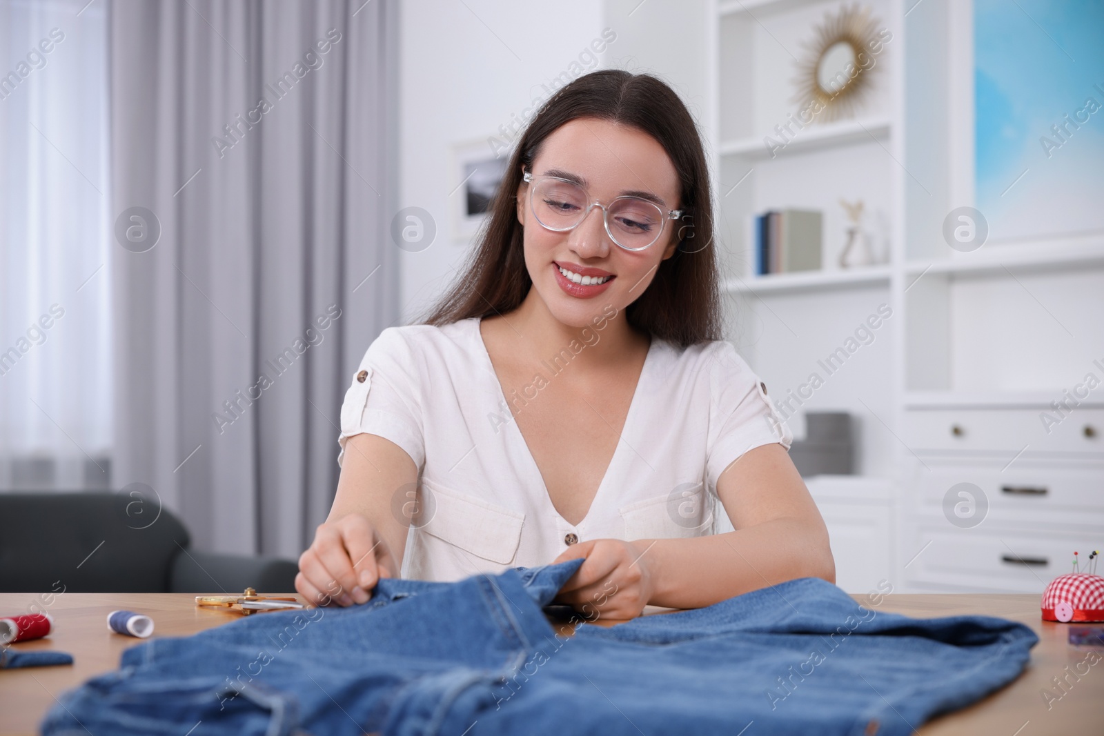 Photo of Happy woman making ripped jeans at table indoors