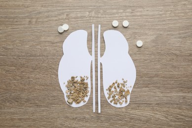 Photo of Paper cutout of kidneys with stones and pills on wooden table, flat lay
