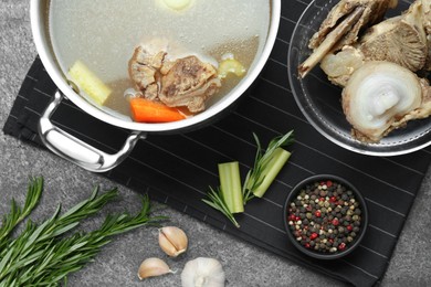 Photo of Pot with delicious bone broth and ingredients on grey table, flat lay