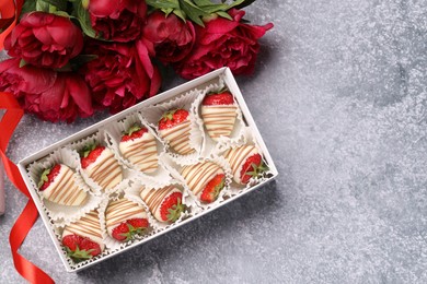 Delicious chocolate covered strawberries in box and flowers on light grey table, flat lay. Space for text