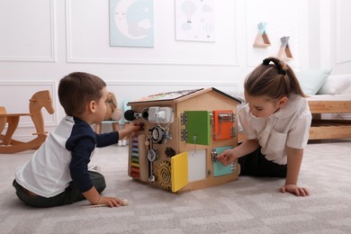 Photo of Little boy and girl playing with busy board house on floor in room