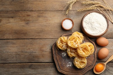 Photo of Flat lay composition with uncooked homemade pasta and ingredients on wooden table. Space for text