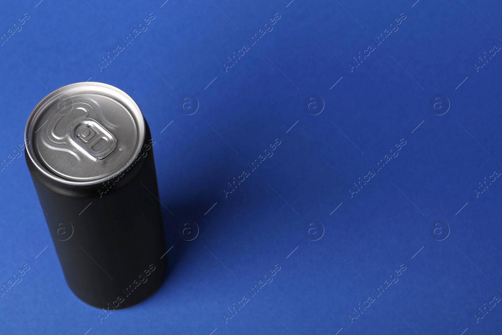 Photo of Energy drink in black can on blue background, space for text