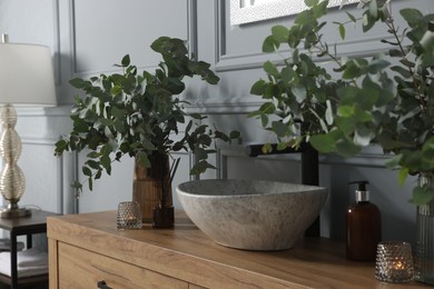 Photo of Eucalyptus branches near vessel sink on bathroom vanity. Interior design