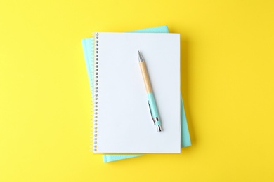 Photo of Notebooks and pen on yellow background, top view