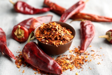 Photo of Bowl with crushed chili pepper and pods on fabric