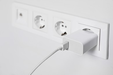 Photo of Charger adapter plugged in power socket indoors, closeup. Space for text