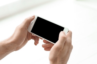 Photo of Man holding mobile phone with blank screen on blurred background, closeup. Mockup for design