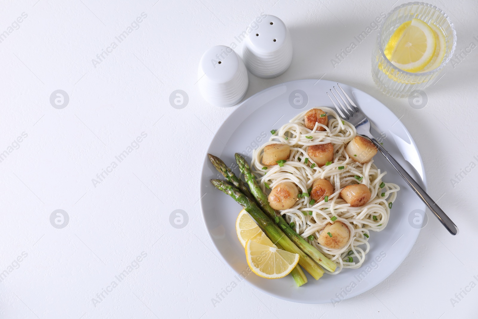 Photo of Delicious scallop pasta with asparagus, green onion and lemon served on white table, flat lay. Space for text