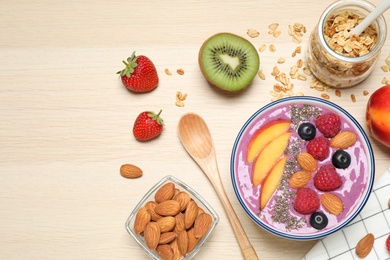 Photo of Delicious acai smoothie with fruits and almonds served on wooden table, flat lay