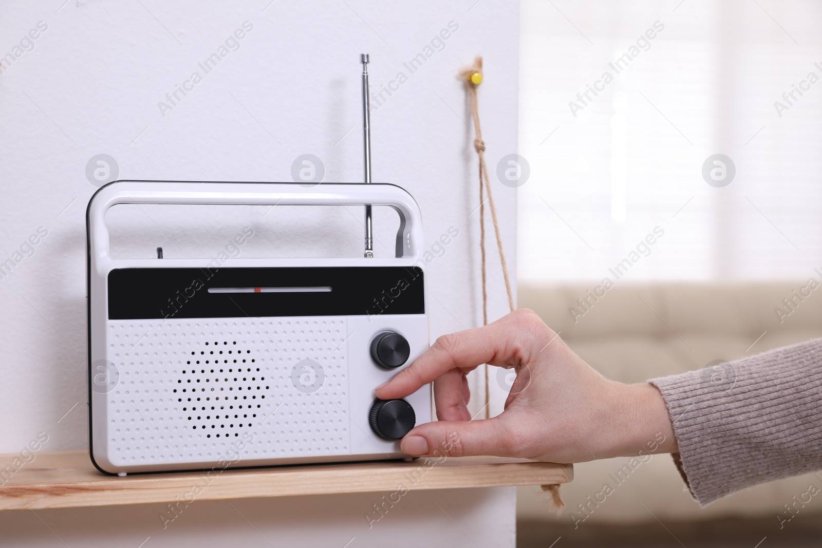 Photo of Woman turning volume knob on radio at home, closeup