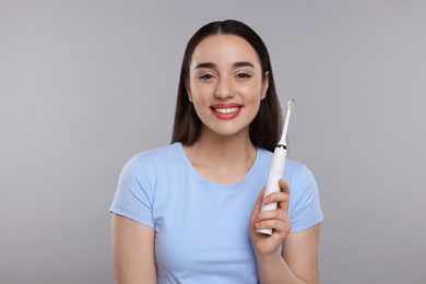 Photo of Happy young woman holding electric toothbrush on light grey background