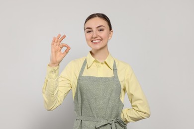 Beautiful young woman in clean apron with pattern on light grey background