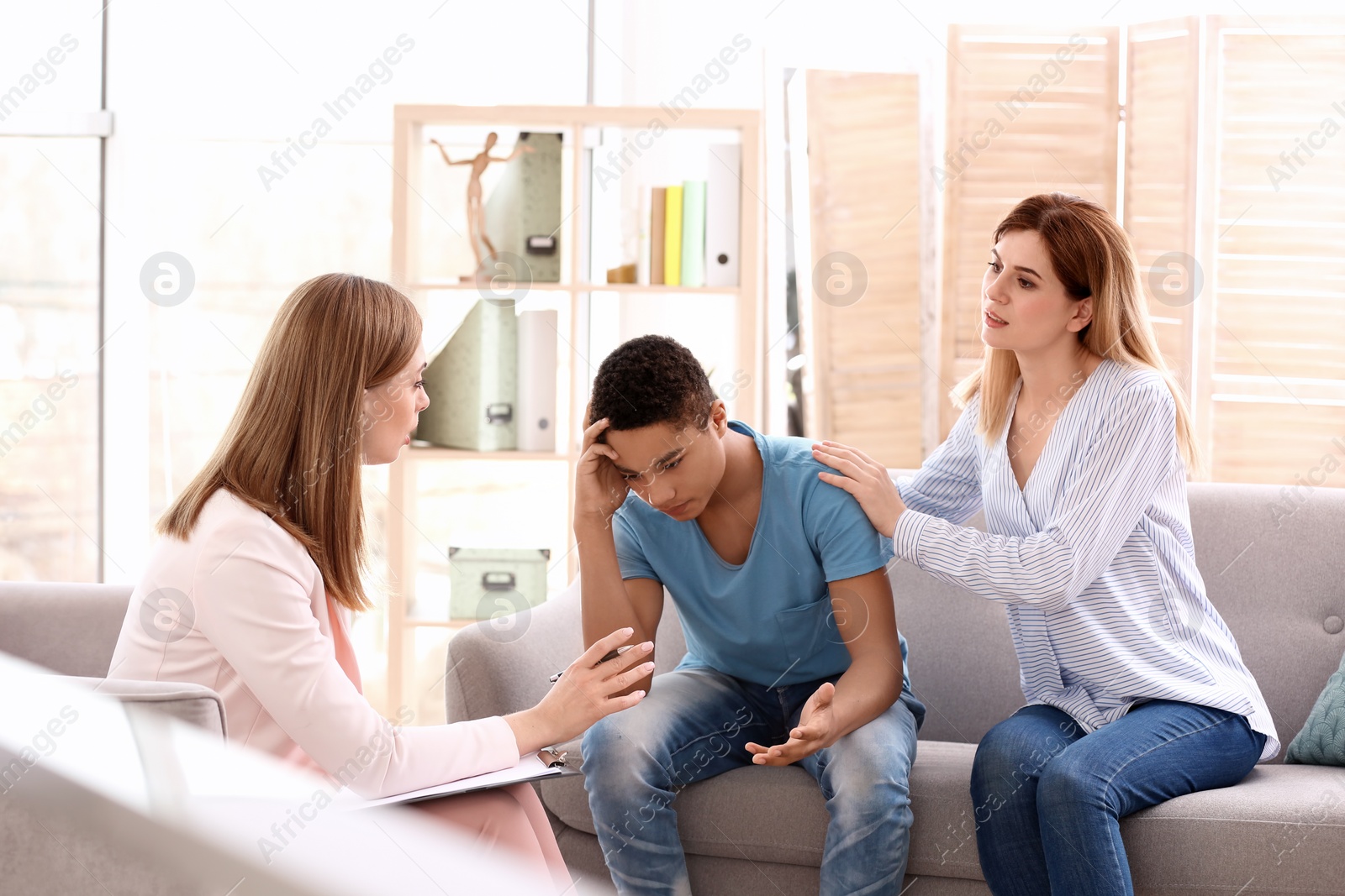 Photo of Young female psychologist working with teenage boy and his mother in office