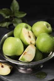 Ripe green apples with water drops and colander on table