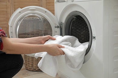 Woman taking clean towel from washing machine in laundry room, closeup