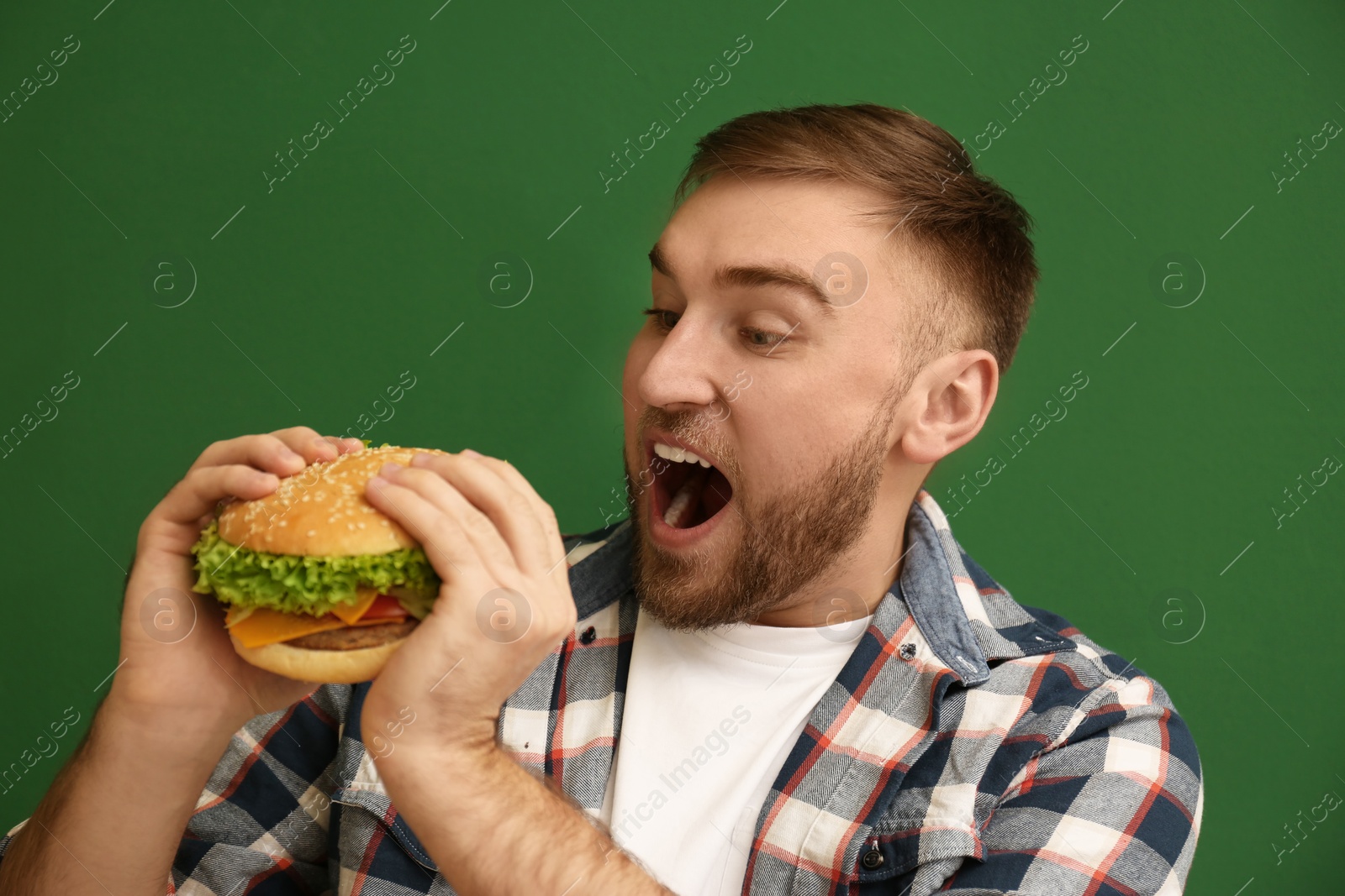 Photo of Young man eating tasty burger on color background