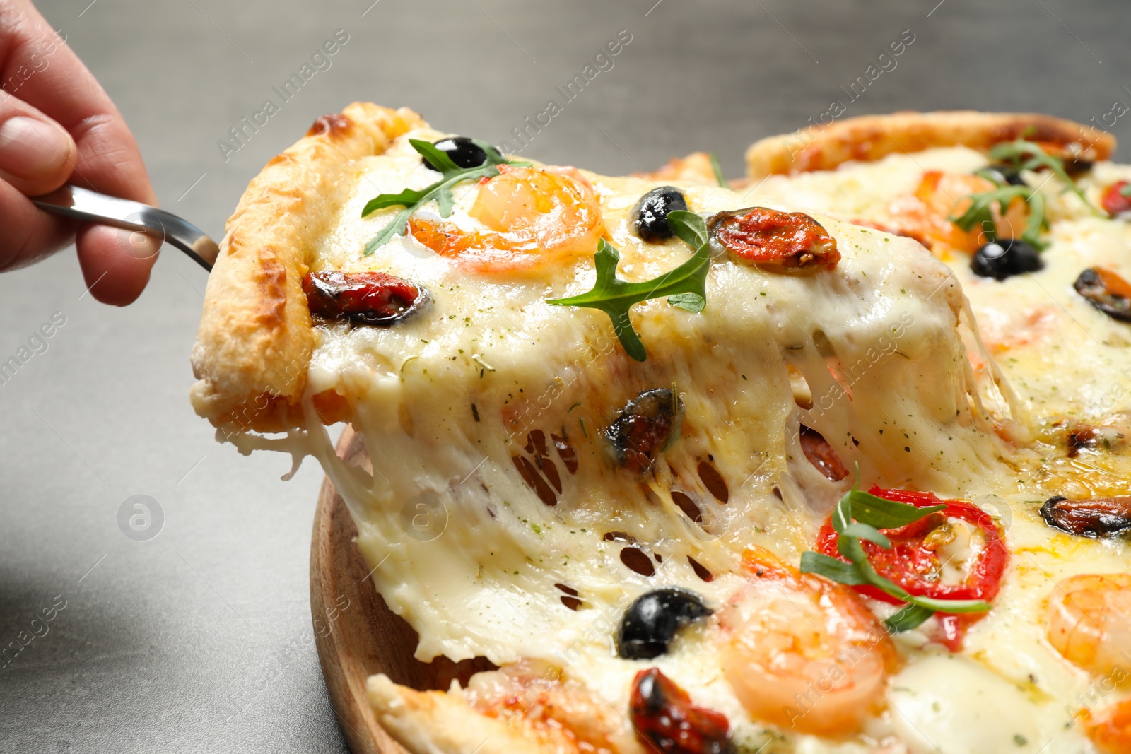 Photo of Woman taking slice of cheese pizza with seafood at table, closeup