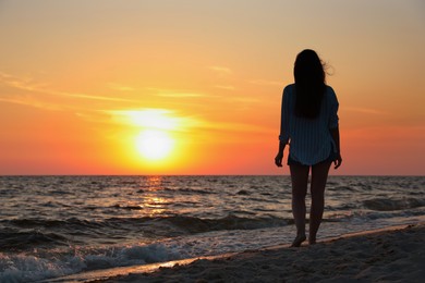 Girl on sandy beach near sea at sunset, back view