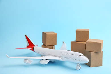 Photo of Airplane model and carton boxes on light blue background. Courier service