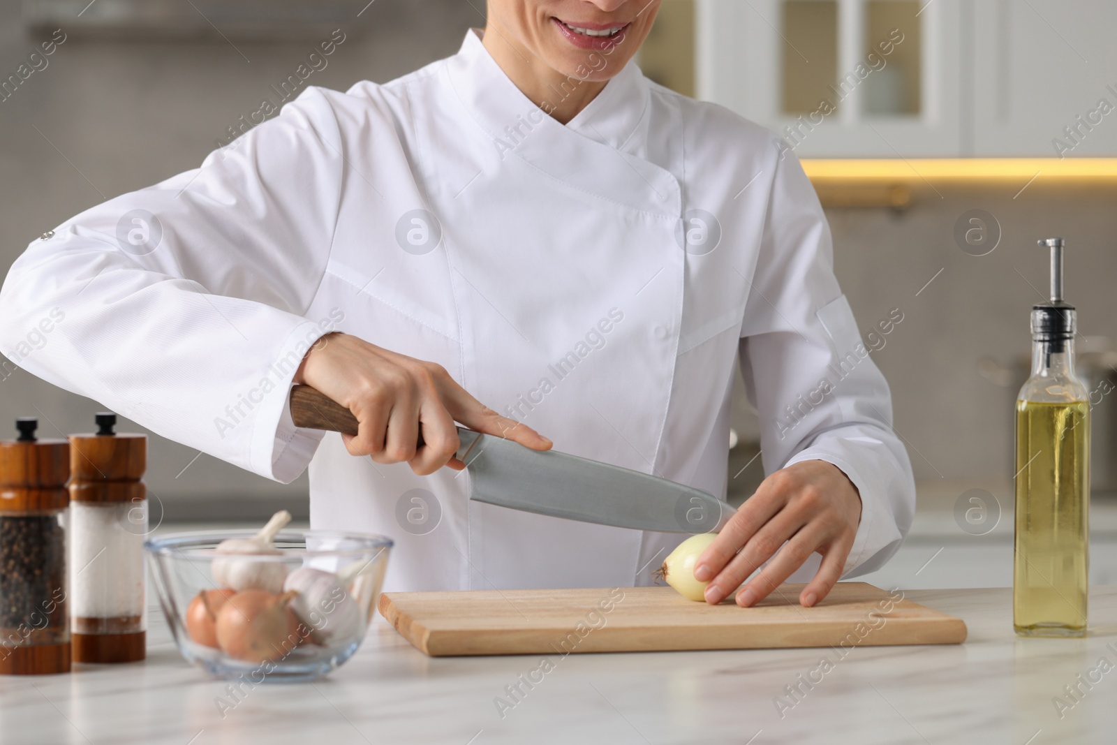 Photo of Professional chef cutting onion at white marble table indoors, closeup