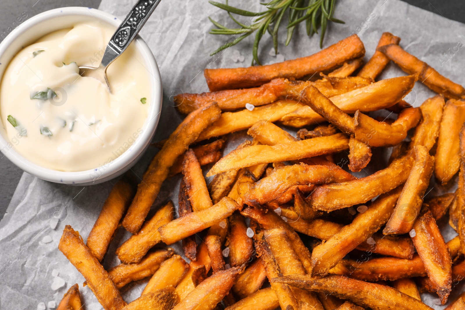 Photo of Delicious sweet potato fries and sauce on parchment paper, closeup