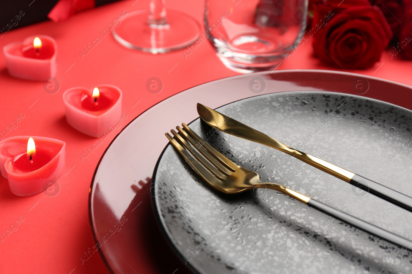 Photo of Place setting with heart shaped candles and bouquet of roses on red table, closeup. Romantic dinner