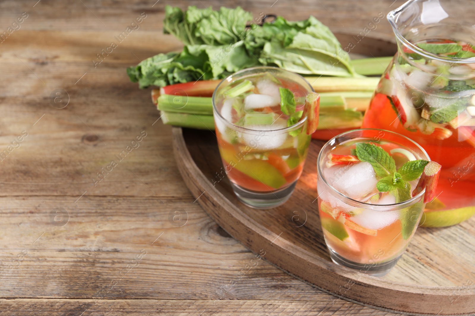 Photo of Glasses and jug of tasty rhubarb cocktail with lime fruits on wooden table, space for text