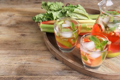 Glasses and jug of tasty rhubarb cocktail with lime fruits on wooden table, space for text