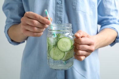 Photo of Young woman holding jar with fresh cucumber water, closeup