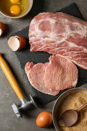 Raw pork chops and ingredients for cooking schnitzel on grey table, flat lay