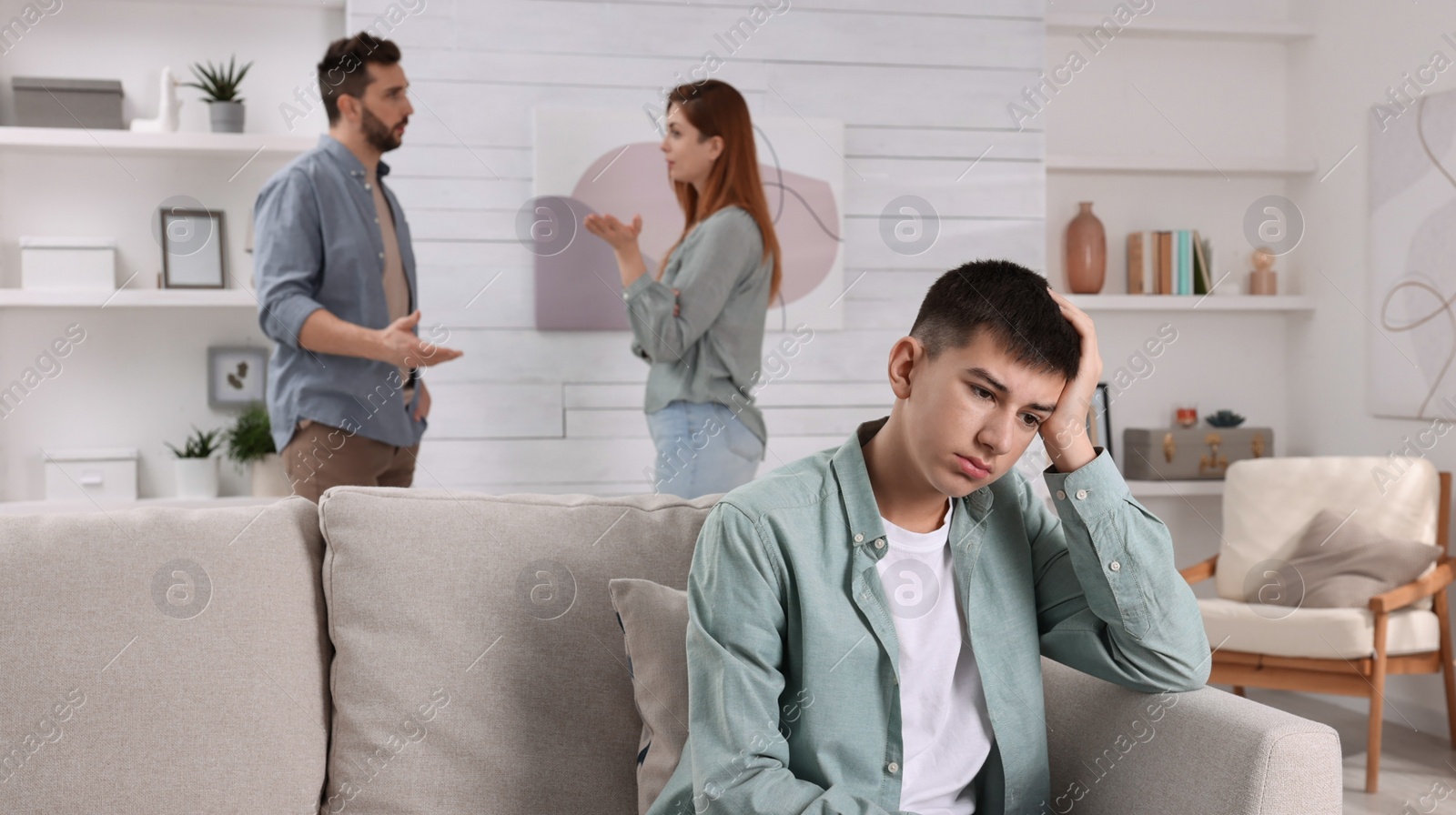 Photo of Couple arguing at home, focus on their unhappy teenage boy. Problems in family