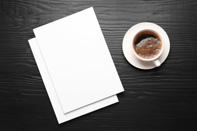Photo of Blank paper sheets for brochure and cup of coffee on black wooden background, flat lay. Mock up