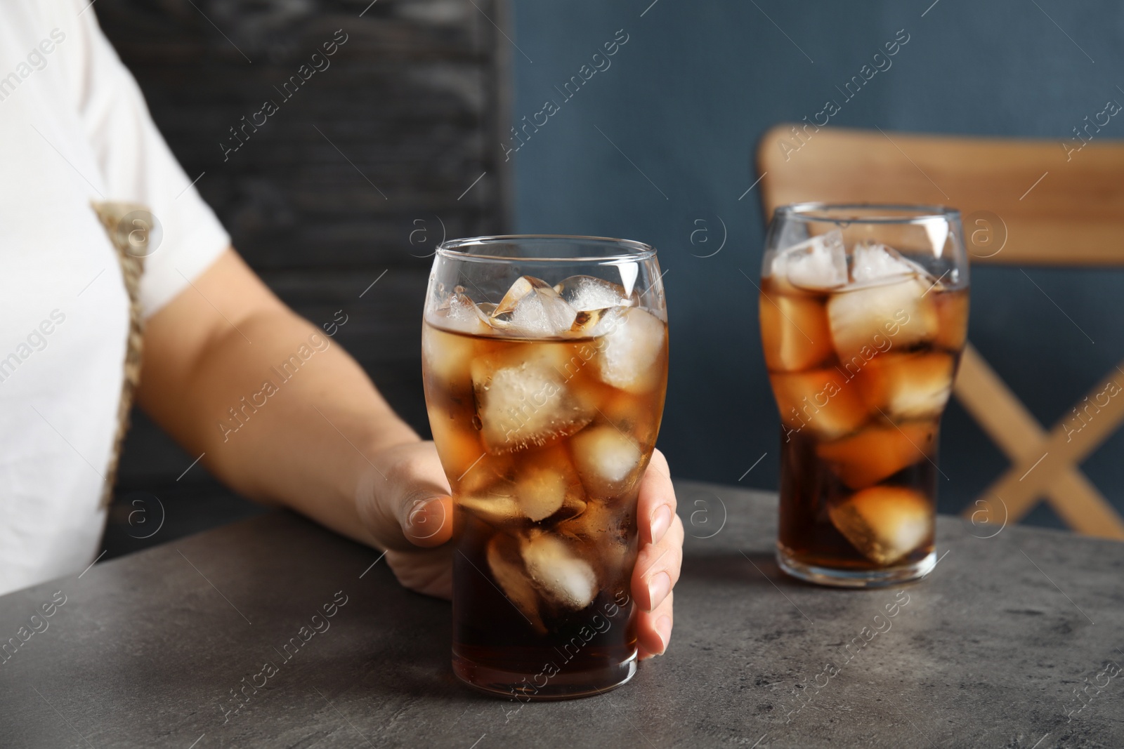 Photo of Woman with glass of tasty refreshing cola at table, closeup view